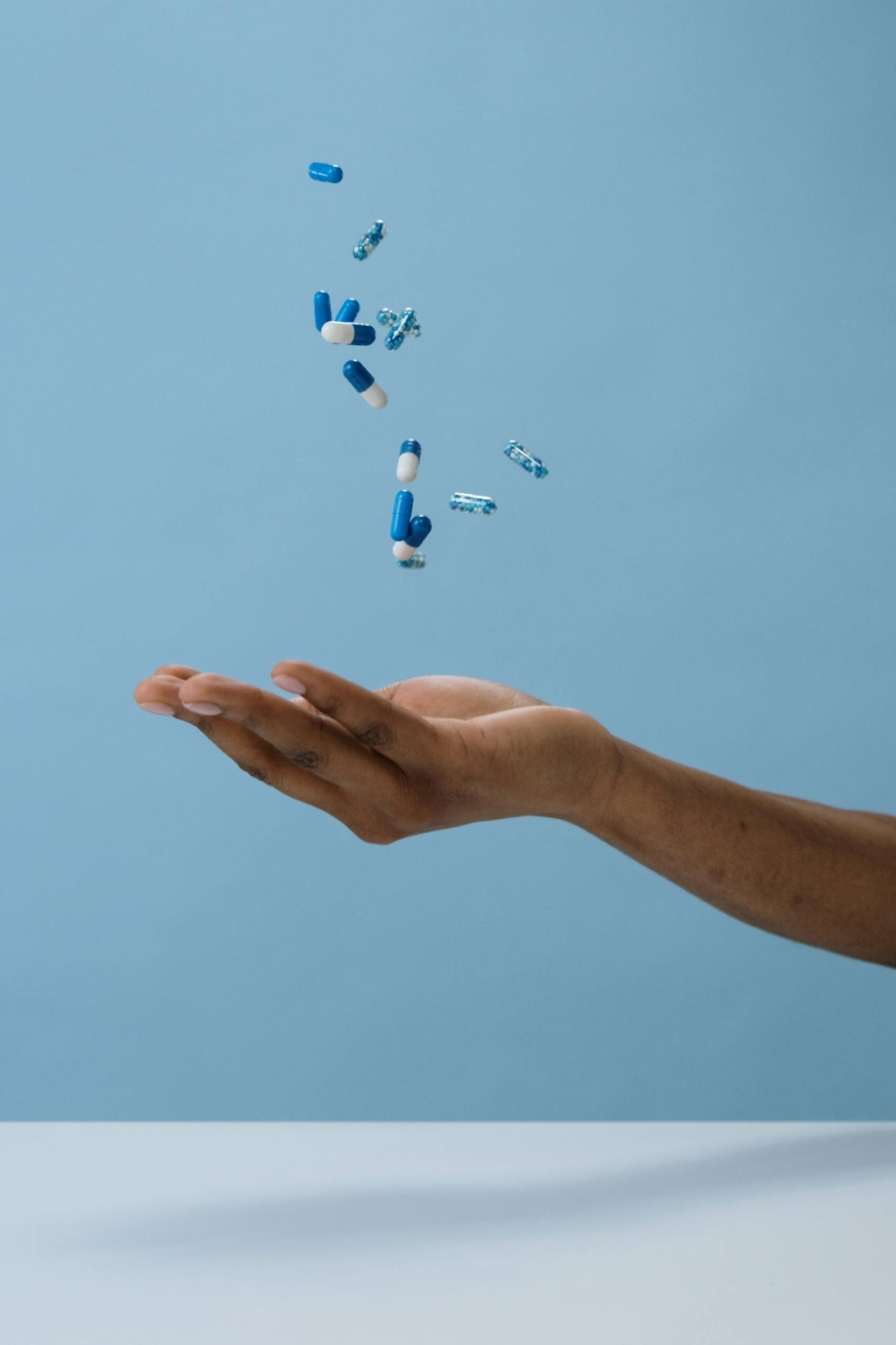 A hand catching blue pills midair against a light background, symbolizing healthcare and medication.