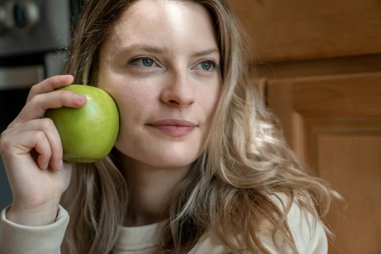 Close-up portrait of a woman indoors holding a green apple, showcasing natural beauty and health.