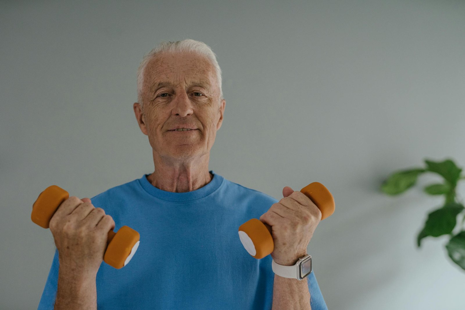 Elderly man in blue shirt lifting dumbbells and smiling indoors, promoting active lifestyle.